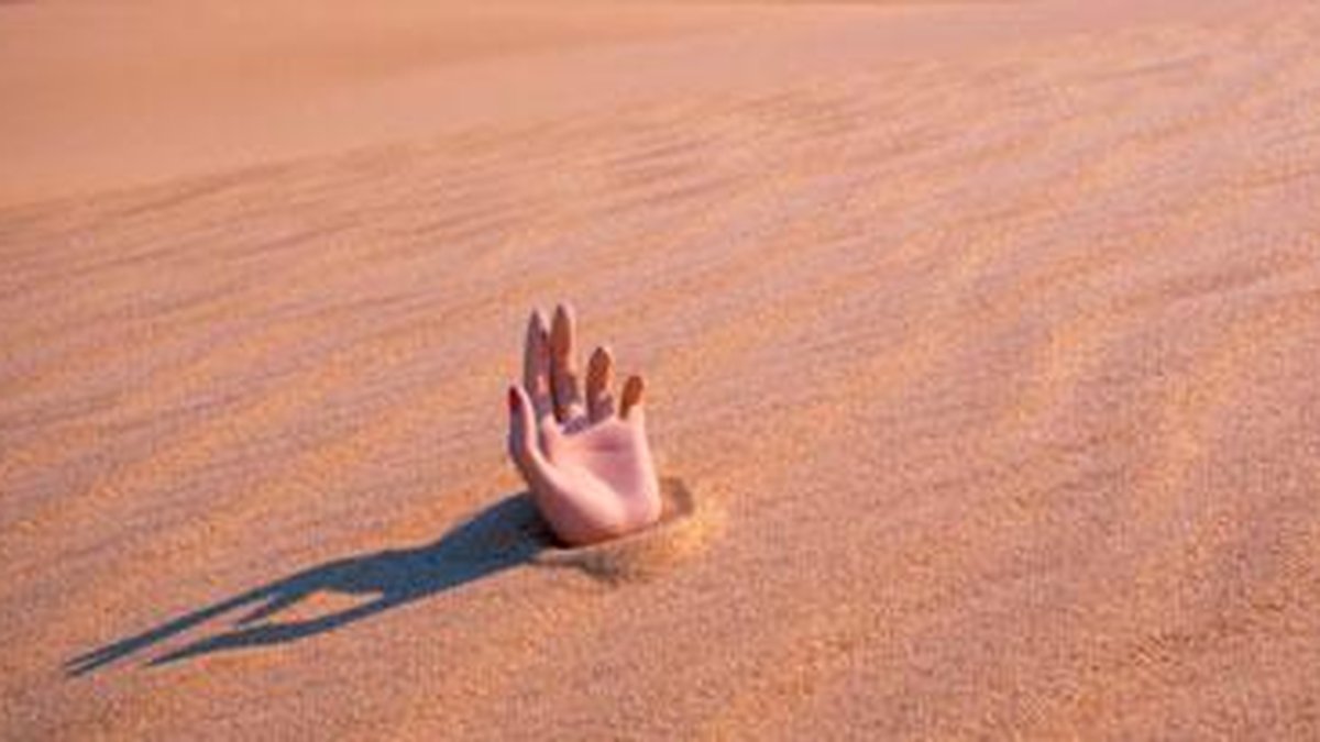 Mão afundando na areia movediça tentando tirar dicas para sobreviver no  deserto enterrado