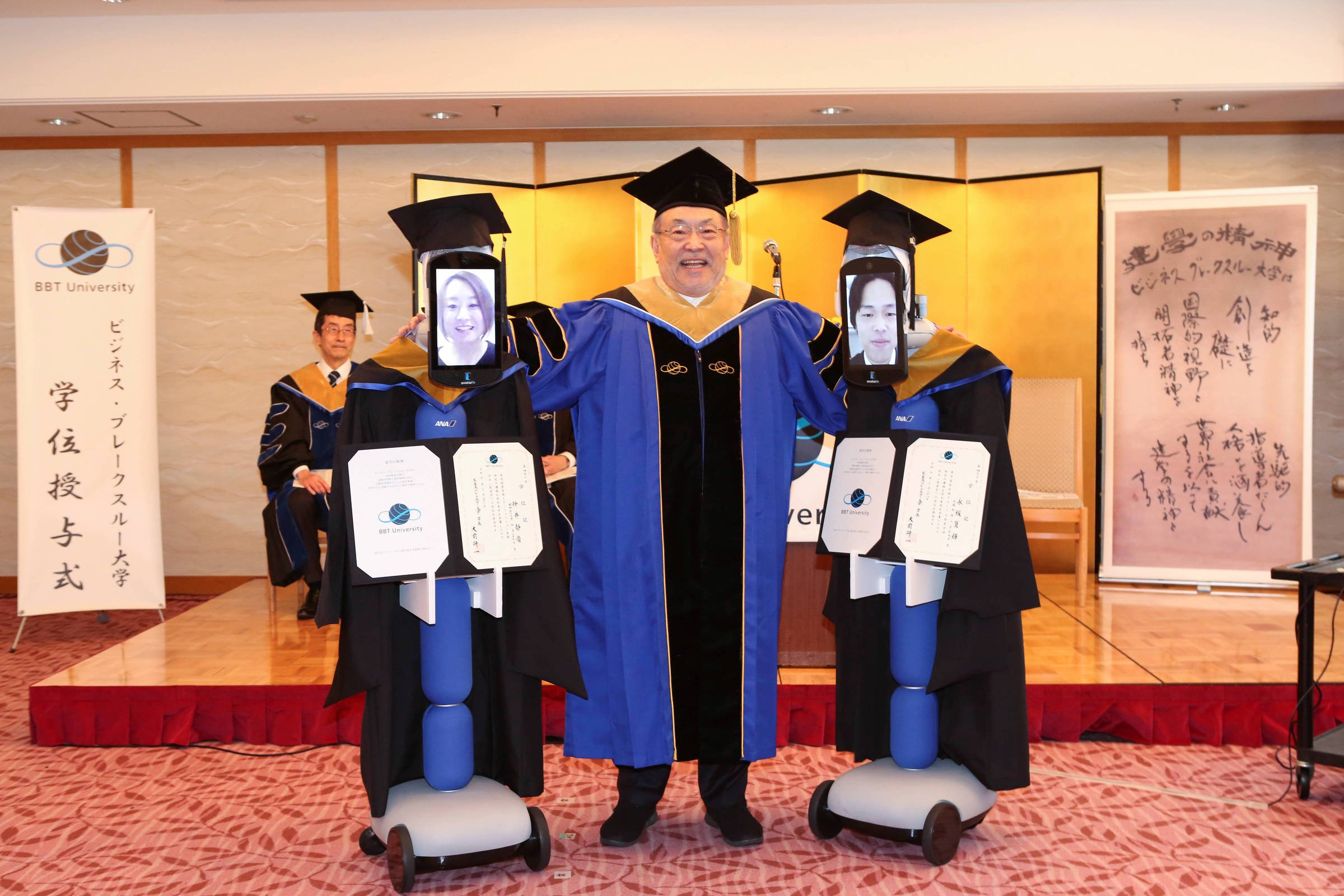 Kenichi Ohmae, presidente da instituição, entrega certificados a alunos representados por robôs