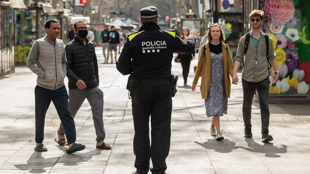 Um policial detém turistas passeando por Barcelona, Espanha, em 15 de março; o país contava então com 1.809 mortos e quase 25 mil contaminados.