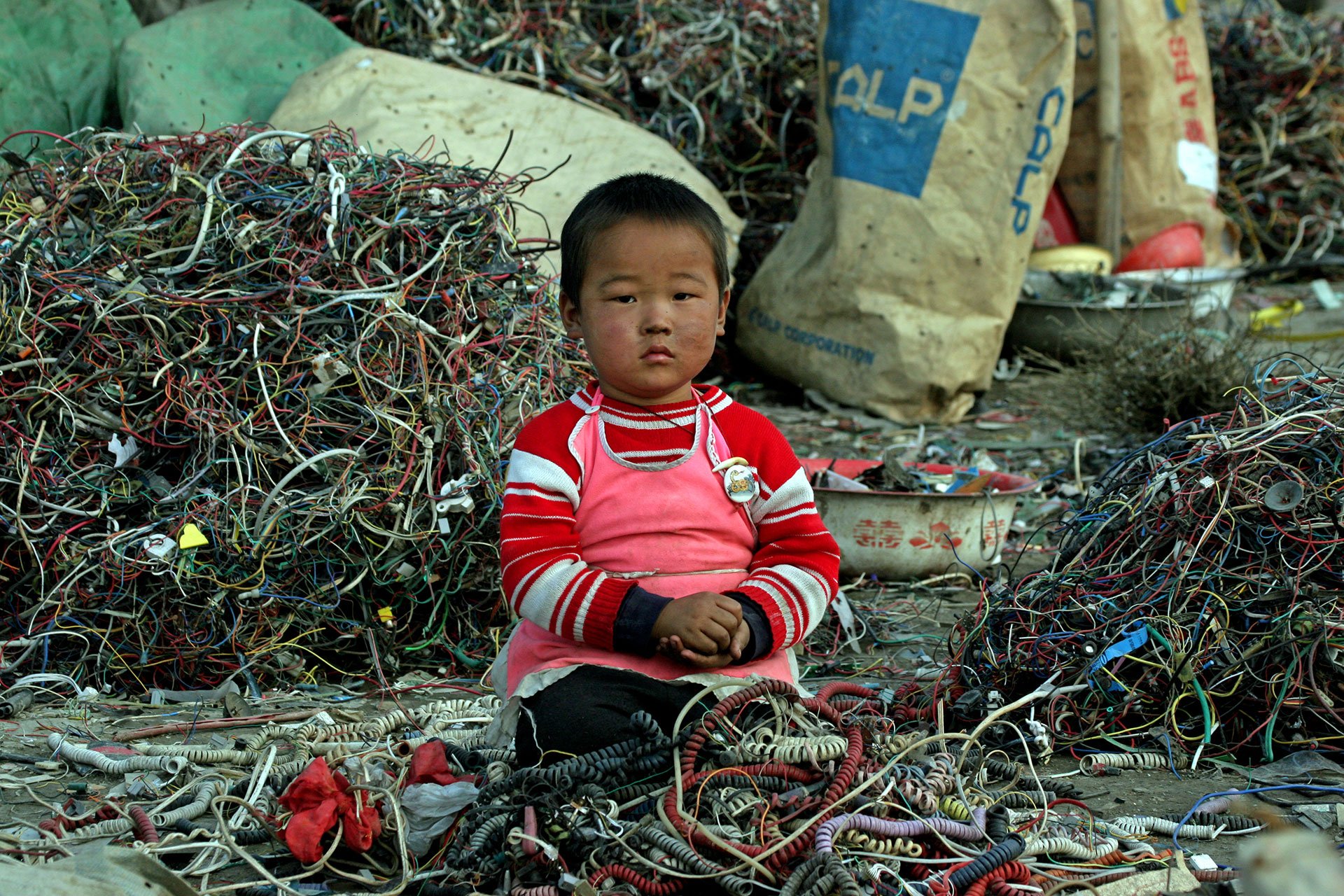Uma criança brinca sentada entre cabos e lixo eletrônico em Guiyu, China.