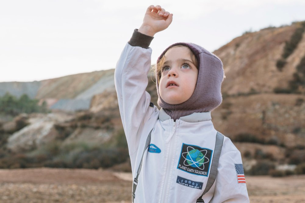 Menina com uniforme de astronauta olha para o céu: nascimentos no espaço podem mudar a história da humanidade.