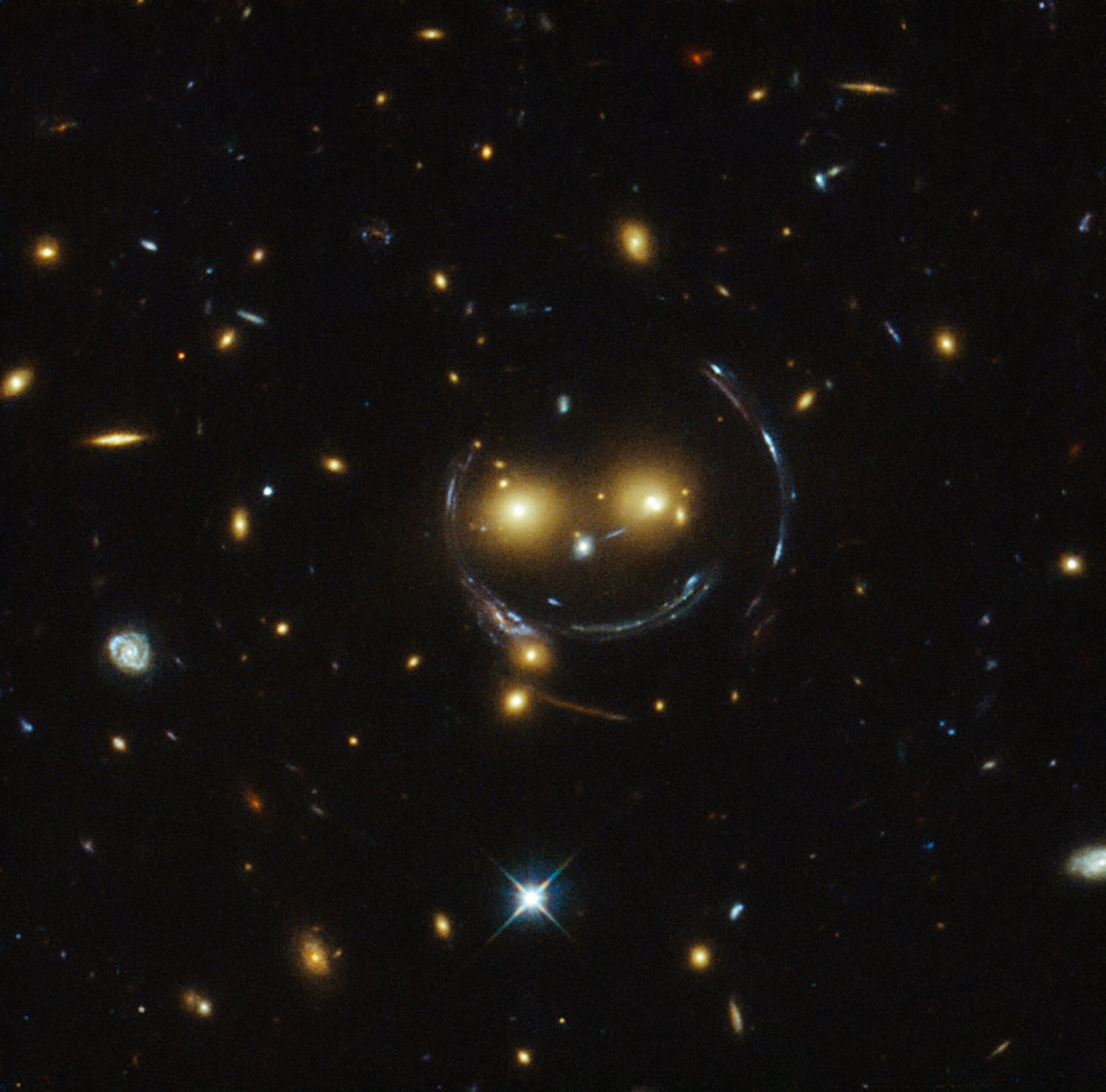 A luz distorcida de uma galáxia ao redor de duas galáxias distantes criam a impressão de um rosto sorridente no espaço.