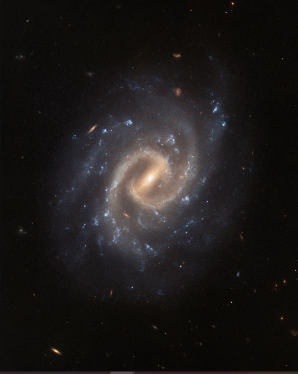 A Galáxia Tranquila apresenta uma 'barra' central brilhante e braços espirais.