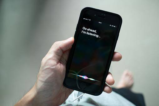Uma pessoa segurando um iPhone, que está na página inicial da Siri.