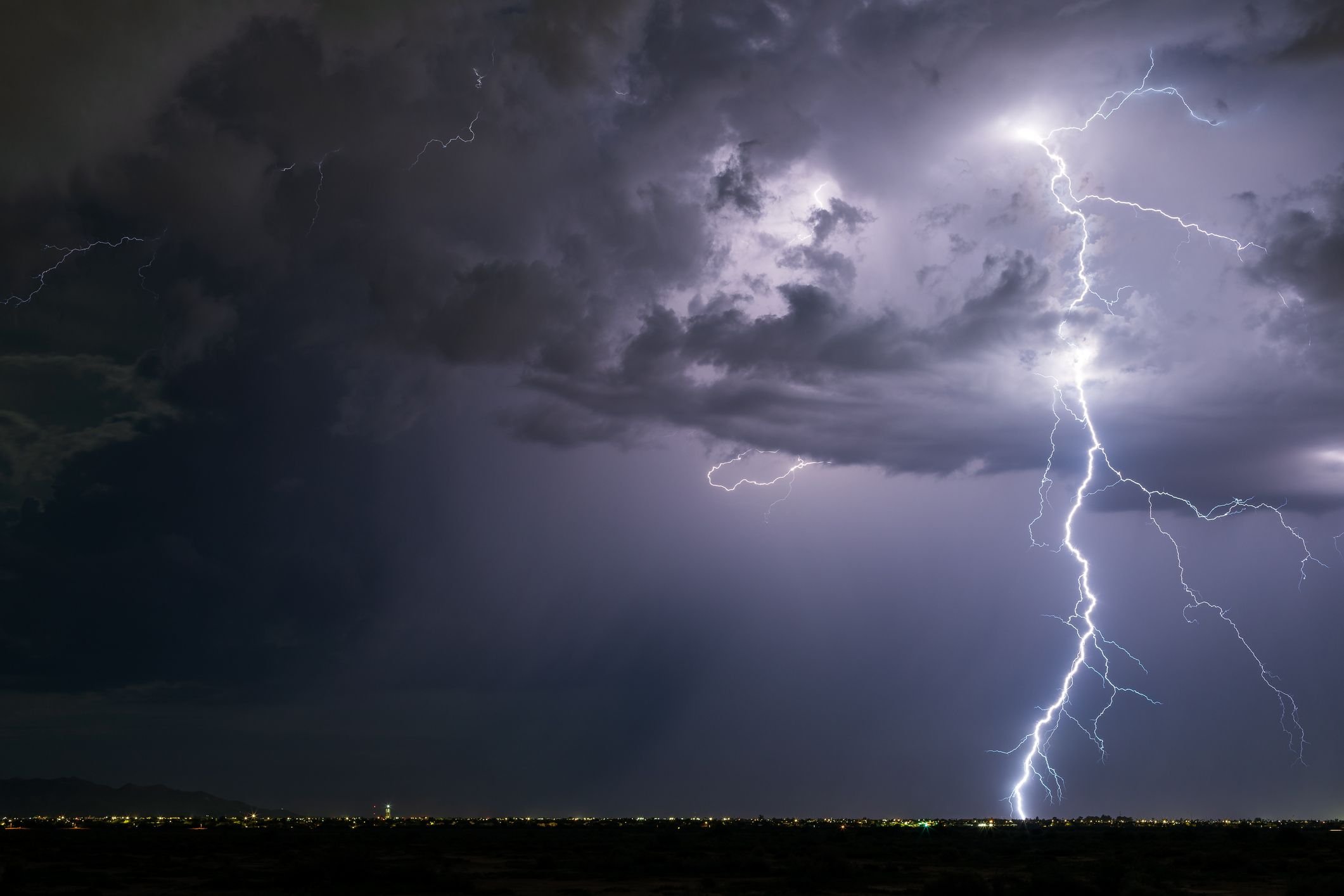 A fotografia apresenta um raio (relampago) saindo de uma nuvem e caindo na superfície da Terra.