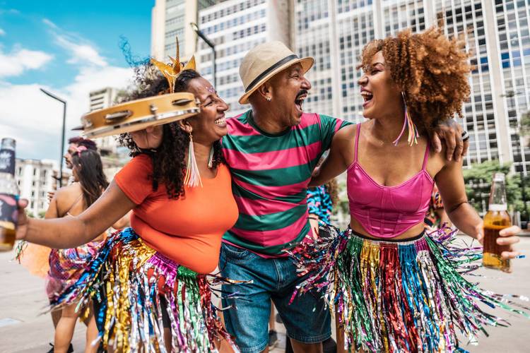 Duas mulheres e um homem curtindo o carnaval em uma cidade como turistas. Eles estão fantasiados com roupas coloridas.