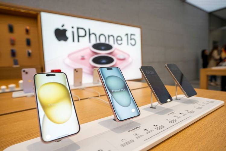 5 iPhones 15 lado a lado. Logo atrás, existe um letreiro do iPhone 15.