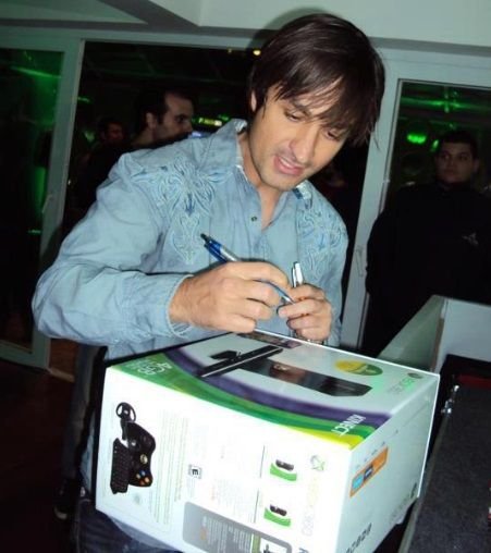 Alex Kipman de pé vestindo uma camisa jeans, assinando a caixa de um console Xbox.