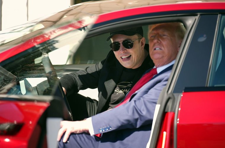 Donald Trump no volante de um carro vermelho da Tesla; Elon Musk está de óculos escuros e boné no banco do passageiro.