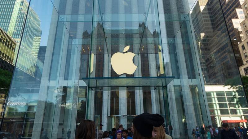 A entrada da Apple Store de Nova York, com a cúpula de vidro transparente com a logo da empresa na frente e algumas pessoas na entrada.