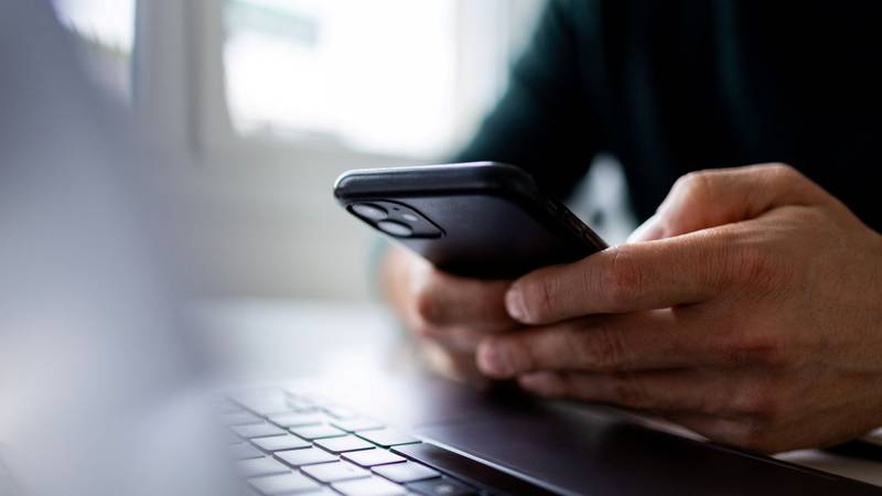 Foto de uma pessoa segurando um iPhone 11 sobre um notebook