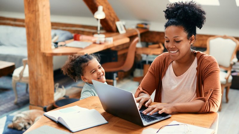 imagem-mostra-uma-mãe-trabalhando-com-laptop-ao-lado-da-filha