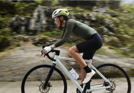Ciclista em uma bike branca, usando camisa verde de manga longa e bermuda preta, usando um smarwatch da Huawei