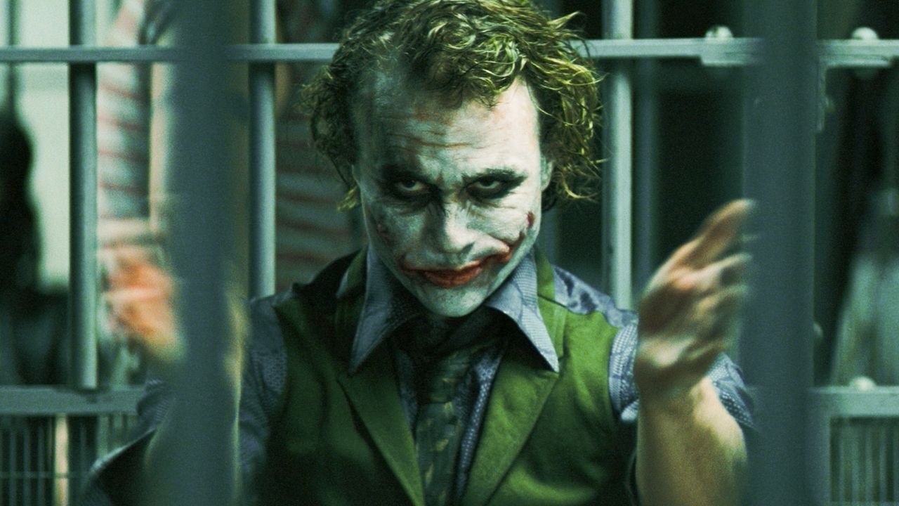 Como assistir aos filmes do Coringa na ordem? Veja lista! O Coringa, o mais famoso vilão do universo do Batman, é uma figura que sempre cativou e intriga o público. Com um histórico de interpretações memoráveis, suas aparições no cinema, tanto como protagonista quanto coadjuvante, se tornaram um marco no mundo dos filmes de super-heróis. A-fotografia-mostra--uma-captura-do-filme-the-dark-knight-o-personagem-coringa-interpretado-por-heath-leadger