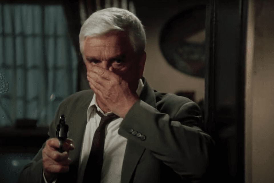 Corra que a Polícia Vem Aí: conheça os clássicos antes de assistir ao remake! Poucos filmes conseguem atravessar gerações e permanecer vivos no imaginário coletivo. A franquia Corra que a Polícia Vem Aí (The Naked Gun), lançada entre o final dos anos 80 e meados dos 90, é um desses raros casos. A-imagem-mosta-o-ator-leslie-nielsen-em-uma-cena-de-corra-que-a-policia-vem-ai